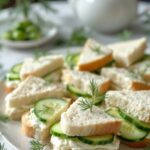 cucumber sandwiches on a plate, along with a tea pot and greenery decoration