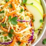 Bowl of cabbage slaow with carrots and apples on a wooden table