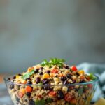 A bowl of quinoa and black bean salad with a slice of lime on a counter