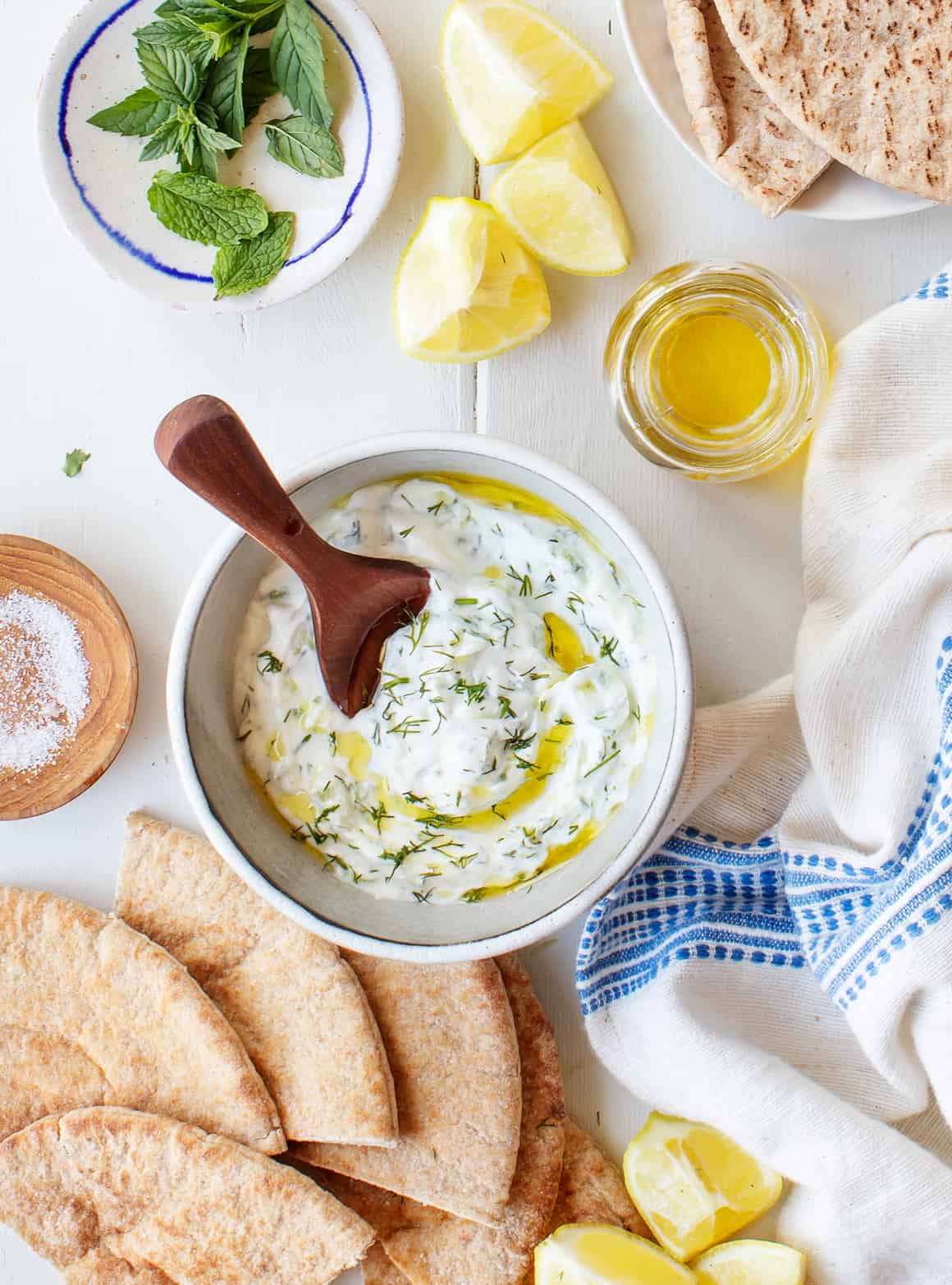 tzatzikiDip A bowl of tzatziki and pitta, small bowl with olive oil and lemon slices on a table