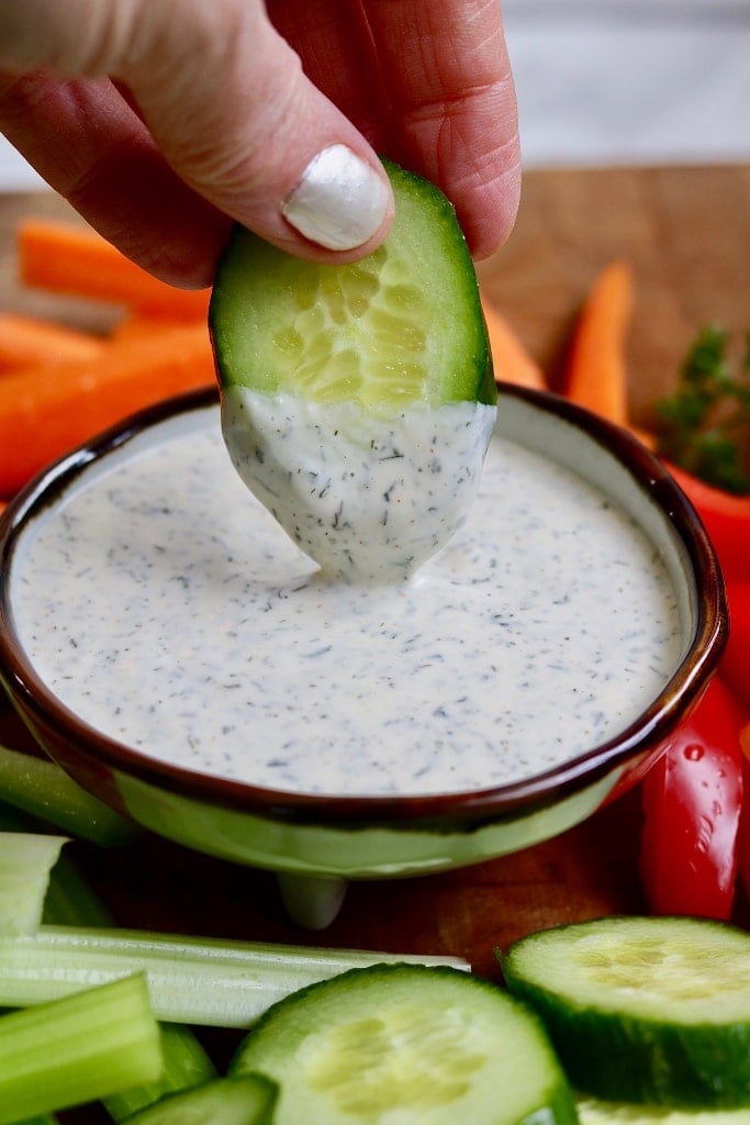 vegan-ranch-dressing Ranch dressing in a bowl and a hand dipping a cucumber slice