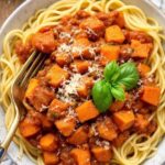 Sweet potato bolognese over pasta on a plate. The plate is on white checkered linen.